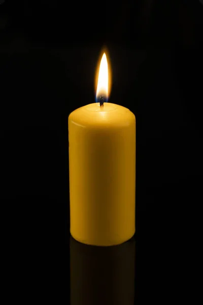 Long, round, yellow wax candles lit on a dark, black background. candle lit — Stock Photo, Image