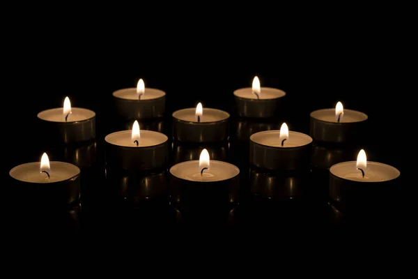 Pequenas velas redondas acesas em um suporte de vela escuro em um fundo preto. velas acesas — Fotografia de Stock