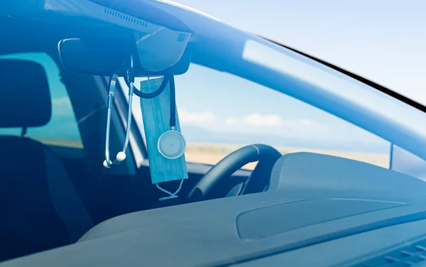 Blue surgical mask and a stethoscope hanging from the rearview mirror of a medical car with the background slightly out of focus. Emergency Doctor Concept by covid 19.