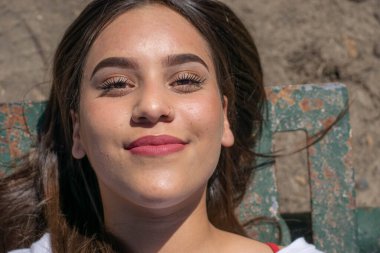 Burnu delinmiş genç bir kız uzanmış gülümsüyor.