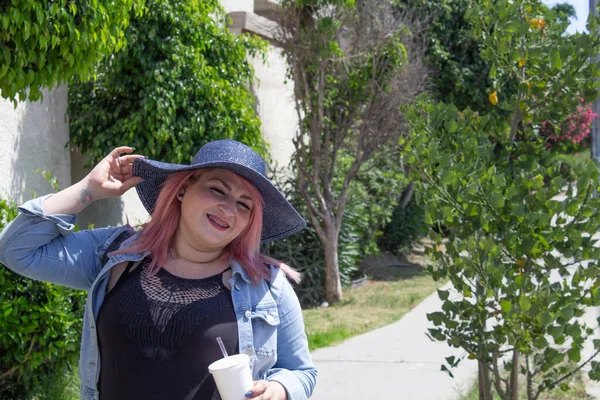夏に公園を歩きながら帽子をかぶった幸せな女性 爽やかなドリンクを飲みながら — ストック写真