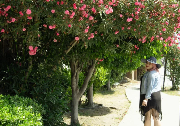 Wanita Bertopi Berjalan Samping Pohon Bunga Merah Muda — Stok Foto