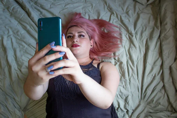 粉红头发的女人用手机躺在床上 — 图库照片