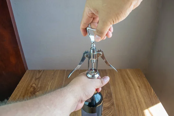 personal perspective of man uncorking bottle of red wine with corkscrew