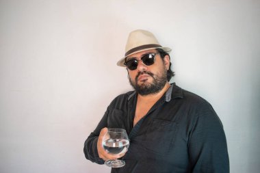 Panama şapkalı İspanyol adam bardağı berrak likörle gösteriyor. Kristal tekila, votka ya da mezcal gibi.