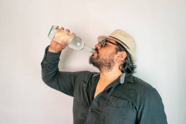 Latin görünümlü bir adam berrak bir likör şişesinden içiyor. Kristal tekila, votka ya da mezcal gibi.