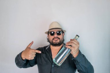 Latin görünümlü bir adam açık likör şişesi gösteriyor. Kristal tekila, votka ya da mezcal gibi.