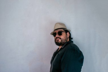 Kameraya bakarken gözlük ve şapka takan sakallı yakışıklı Latin adam.