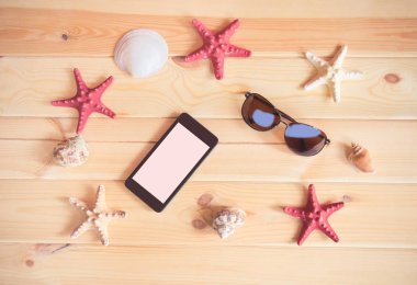 Yaz tatil kavramı. Güneş gözlüğü, smartphone, starfishes ve kabukları ahşap arka plan üzerinde.