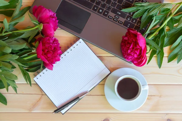 Kahve fincanı, laptop klavye, boş defter ve ahşap masa kırmızı şakayık çiçekleri. Üstten görünüm, kopya alanı.