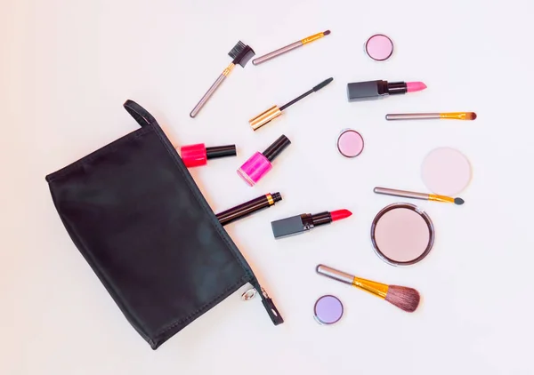 Black makeup bag with cosmetic beauty products spilling out  to pastel colored surface