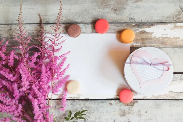 Güzel pembe astilbe çiçekler, hediye kutusu, macaroons ve ahşap arka plan üzerinde metni boş oyun kağıdı