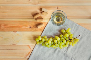 Bir bardak beyaz şarap, şarap mantarlar ve ahşap masa üzerinde üzüm şube. Üstten görünüm, kopya alanı.