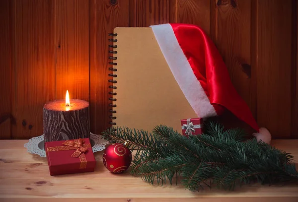 Leeres Notizbuch Tannenzweig Weihnachtsmütze Kerze Weihnachtskugel Und Geschenke Auf Dem — Stockfoto