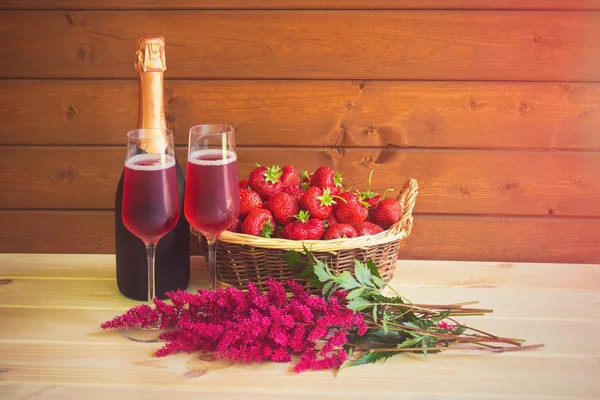 Due bicchieri di champagne rosa, bottiglia di champagne rosa, fiori astilbe e fragola fresca nel cestino di vimini . — Foto Stock