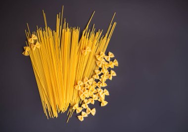 Pişmemiş makarna spagetti ve farfalle koyu arka plan üzerinde. Kopya alanı ile üstten görünüm.