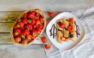 Taze çilek ve taze çilek ve çikolata syrop yaşında tahta masada krep ile hasır sepet. Üstten görünüm.