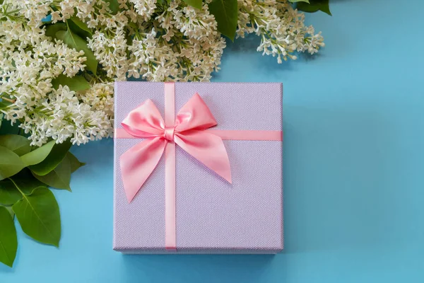 礼品盒与粉红色的弓和白色丁香的花在蓝色背景 顶部视图 复制空间 — 图库照片
