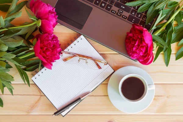 Boş defter, gözlük, laptop klavye, ahşap masa kahve ve kırmızı Şakayık çiçekleri fincan. Üstten Görünüm, kopya alanı.