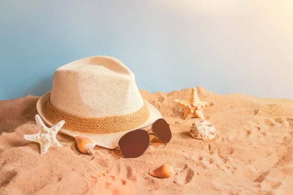 Şapka, güneş gözlüğü, starfishes ve kabukları üzerinde kum mavi zemin üzerine. 
