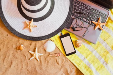 Şapka, dizüstü bilgisayar ve starfishes ve kum plajı üzerinde kabukları ile smartphone. 