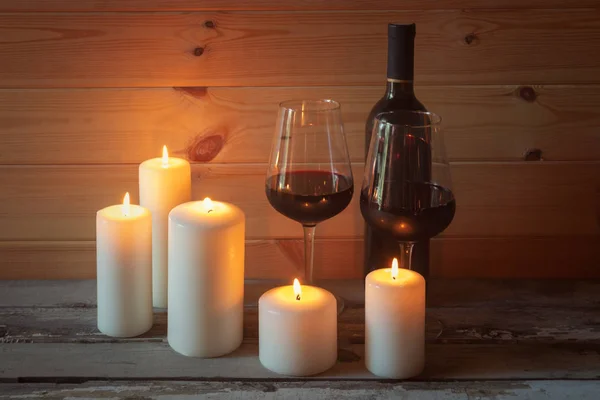 Bottle of red wine, glasses of red wine and candles on aged wooden table. — Stock Photo, Image