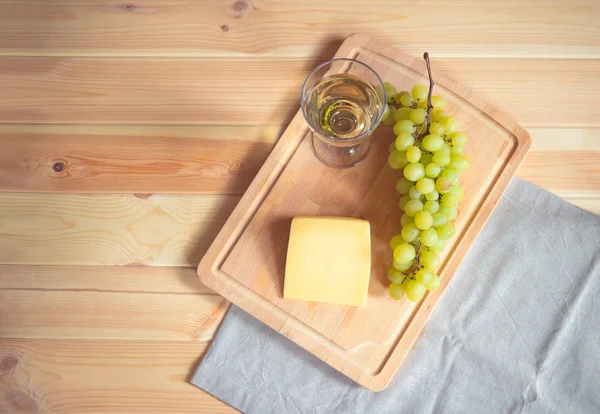 Glass of white wine, parmesan cheese and grape branch on cutting board on wooden background. — Stock Photo, Image