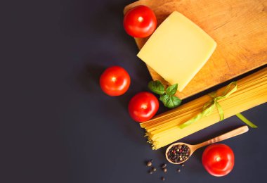 Peynir, biber, taze domates ve fesleğen ile çiğ spagetti makarna koyu arka planda yaprakları. 