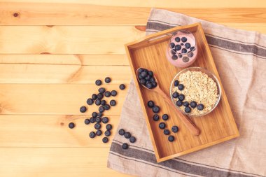 Ahşap masada kase ve yaban mersini yoğurt üzerinde yaban mersini ile yulaf gevreği.
