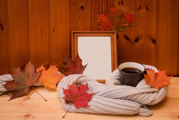 Marco de madera vacío, taza de café envuelto en una bufanda de lana gris y hojas coloridas de otoño —  Fotos de Stock