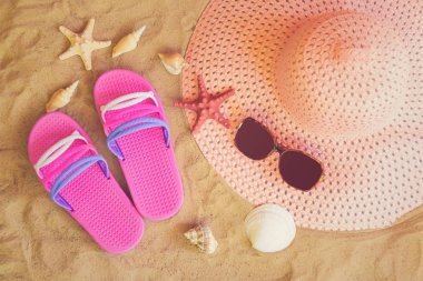 Kum sahilde şapka, flip foplar ve deniz kabukları.