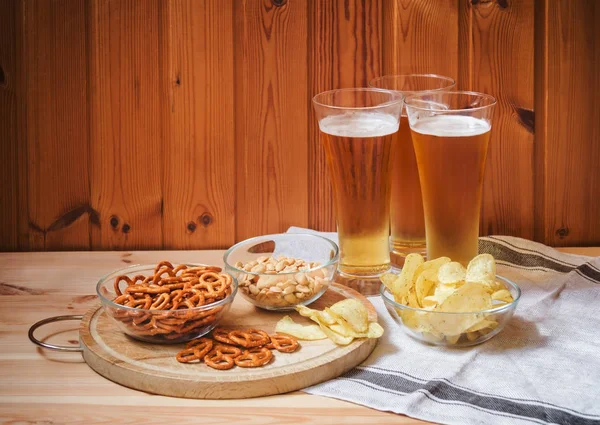 Cerveza ligera con pretzels salados, papas fritas y cacahuetes en mesa de madera . — Foto de Stock