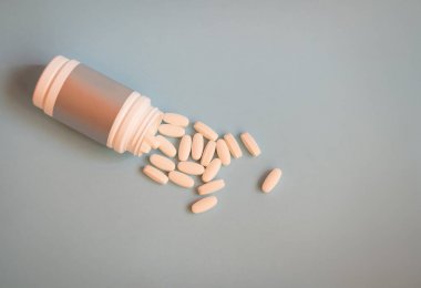 Şişeden mavi arka plana dökülen ilaç hapları. 