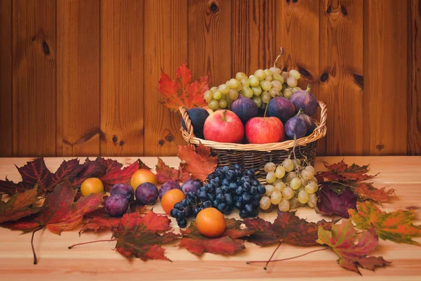 Panier en osier fruits frais et feuilles d'érable d'automne sur fond bois . — Photo