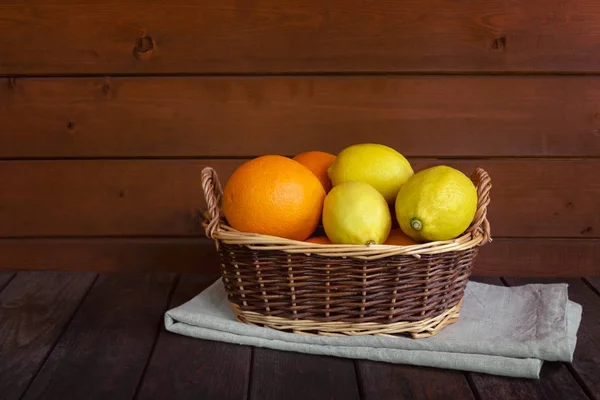 Cesta de mimbre con naranjas frescas maduras y limones sobre mesa de madera envejecida . —  Fotos de Stock