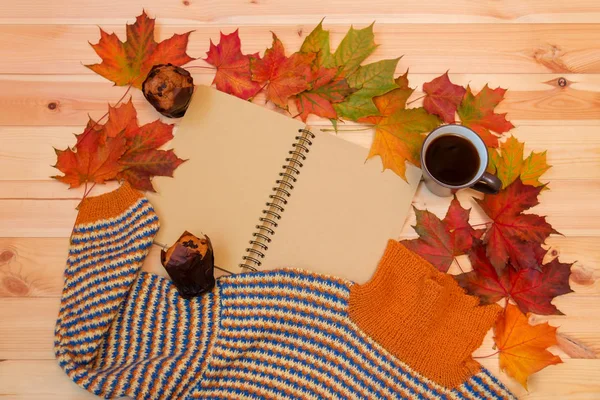 Taza de café caliente, cuaderno vacío, hojas de arce de otoño, magdalenas y suéter casero caliente . — Foto de Stock