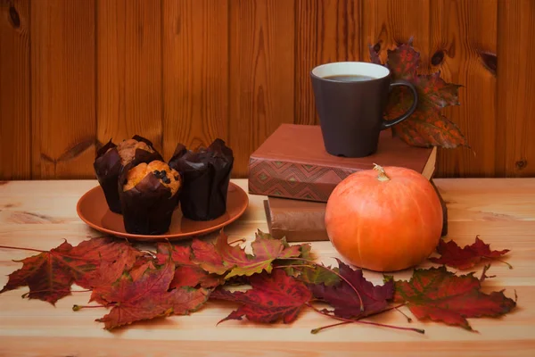 Cafea, frunze de arțar de toamnă, dovleac, cărți și brioșe de vanilie pe masă de lemn . — Fotografie, imagine de stoc