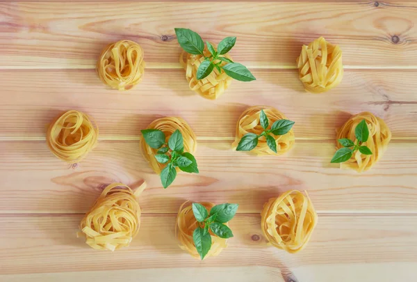 Lebensmittelmuster aus Tagliatelle-Pasta mit grünen Basilikumblättern. — Stockfoto