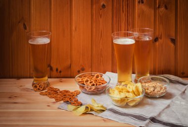 Ahşap masada tuzlu kraker, patates cipsi ve yer fıstığı ile hafif bira üç bardak. 