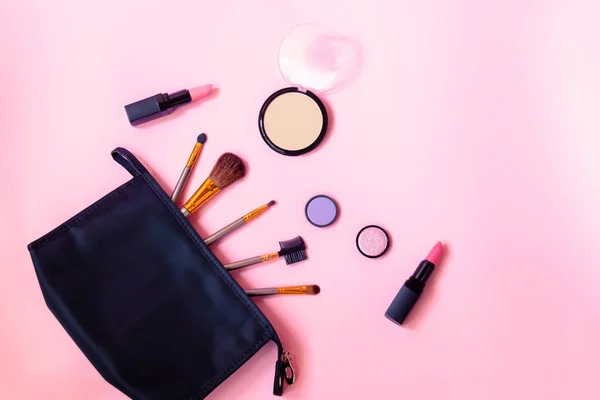 Borsa trucco nera con prodotti cosmetici di bellezza e pennelli per il trucco su sfondo rosa . — Foto Stock