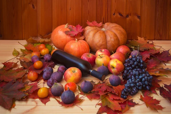 Citrouilles, bouteille de vin rouge, feuilles d'érable d'automne colorées et fruits frais sur table en bois. Concentration sélective . — Photo