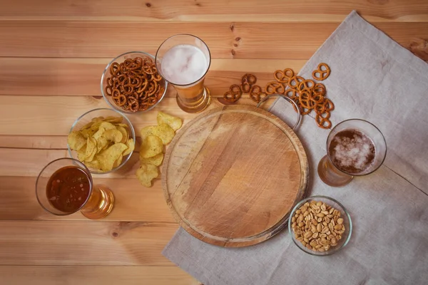 Легкое пиво с солеными крендельками, картофельными чипсами и арахисом на деревянном столе . — стоковое фото