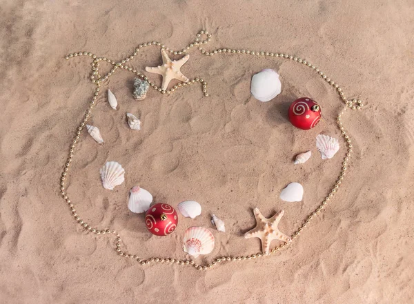 Frame made of christmas balls, beads, starfishes and seashells on sand beach. — Stock Photo, Image