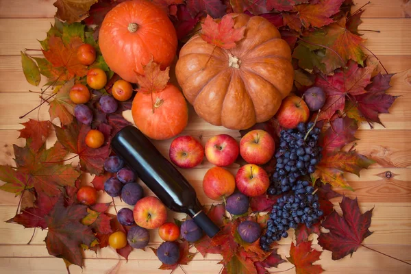 Citrouilles, bouteille de vin rouge, feuilles d'automne et fruits frais sur table en bois . — Photo