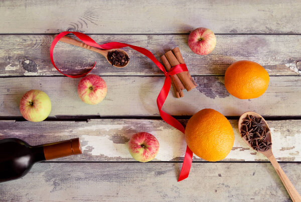 Mulled wine recipe ingredients. Bottle of red wine, oranges, cinnamon sticks, anise, cloves and apples on aged wooden background. 