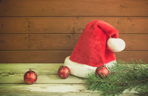 Fluffy Santa hat, christmas balls and pine branches on aged wood  table. Toned image. — Stock Photo, Image