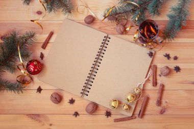 Empty notebook, fir branches, glass of mulled wine, christmas decorations, spices and walnuts on wooden background.