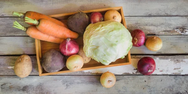 Surtido de verduras frescas en bandeja de madera y verduras frescas cerca de la mesa de madera envejecida . —  Fotos de Stock