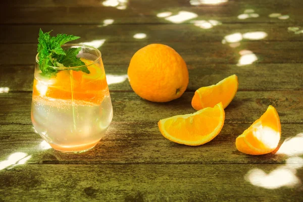 Cold summer orange lemonade in glass on rustic wooden table. Fresh oranges near. Selective focus.
