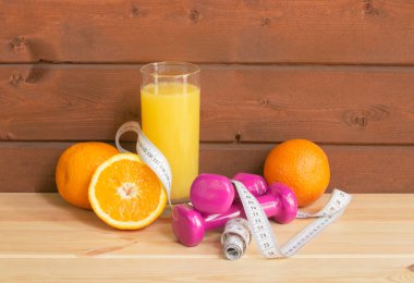 Bir bardak portakal suyu, taze portakallar, dambıllar ve tahta masanın üzerindeki mezura. Seçici odaklanma. Sağlıklı beslenme ve zindelik kavramı. Kopyalama alanı ile göster.